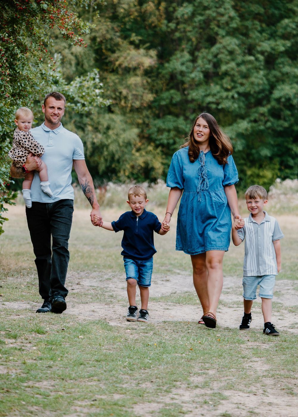 Family Photoshoot - Family members walk together along dirt path through green woodland setting.