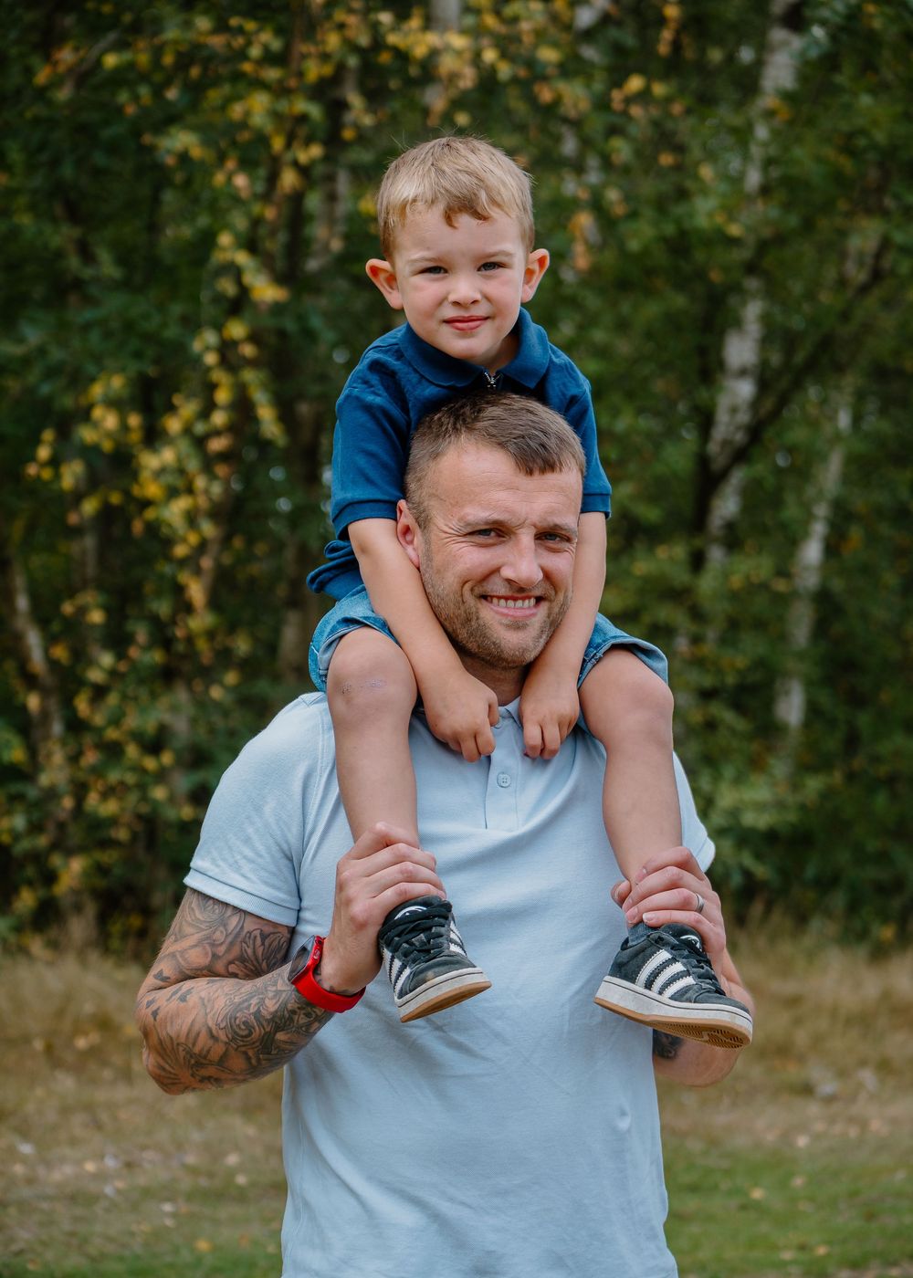 Family Photoshoot - Parent gives child shoulder ride while smiling outdoors in wooded area.