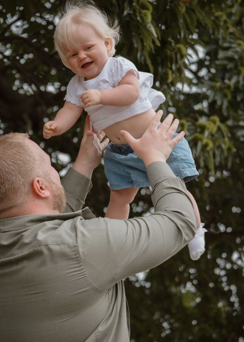 Family Photoshoot - Cusworth Hall - Parent lifts and plays with small child wearing denim shorts outdoors.