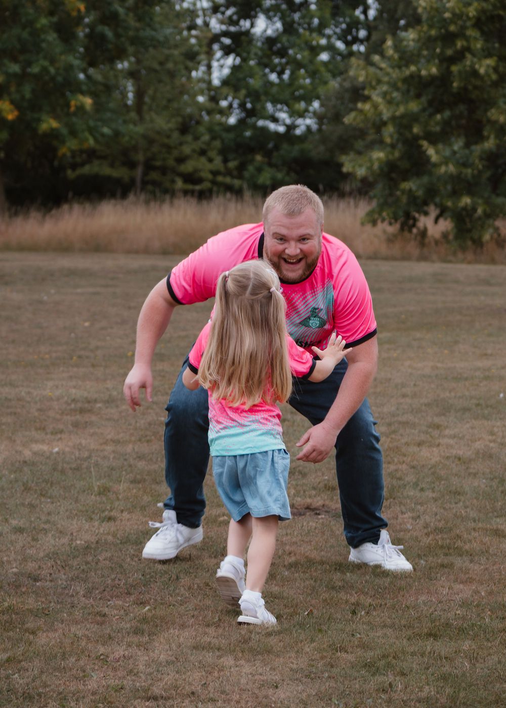 Family Photoshoot - Cusworth Hall - Parent in pink shirt plays chase with child in blue outfit on grass.