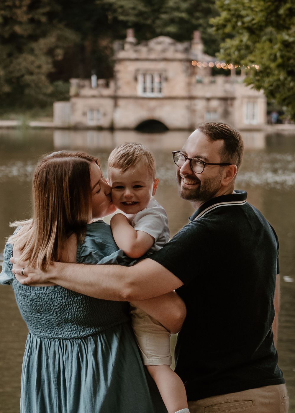 Family Photoshoot - Newmillerdam - Family sharing an intimate moment by a lake with historic architecture in the background.