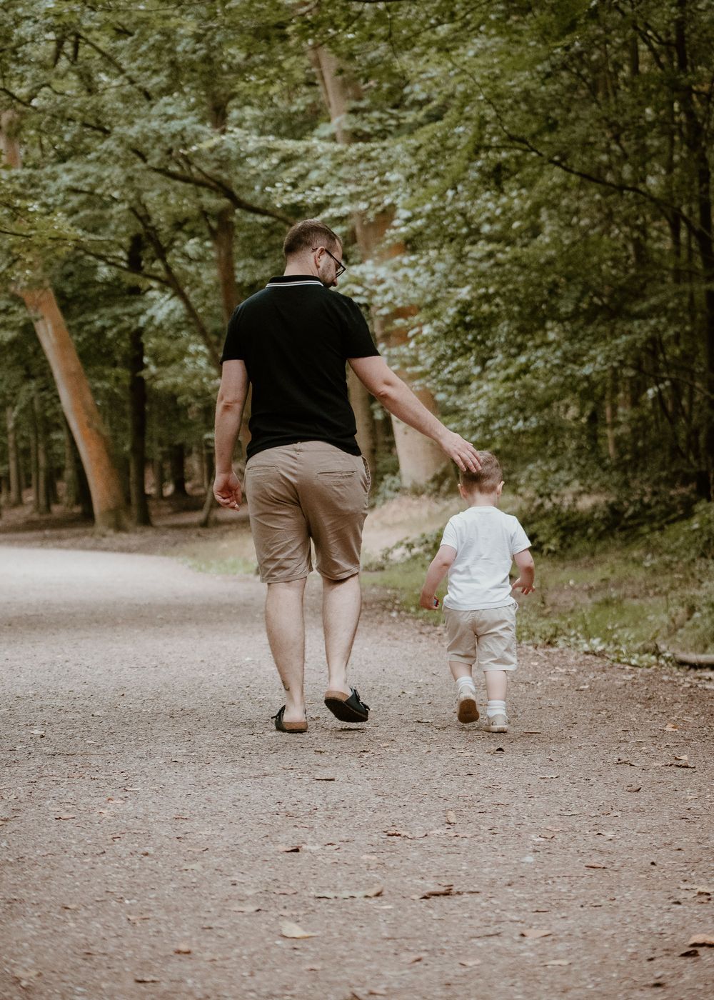 Family Photoshoot - Newmillerdam - Parent and child walking hand in hand down a tree-lined path on a sunny day.