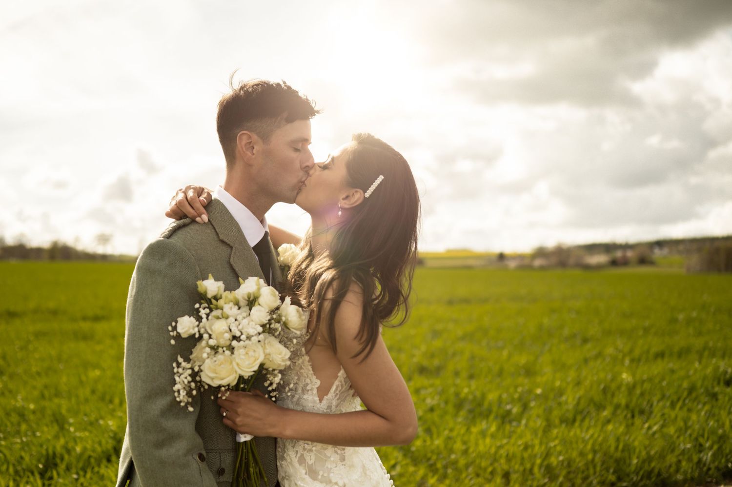 A couple shares a romantic moment at sunset in a lush green field with a bouquet of white flowers.