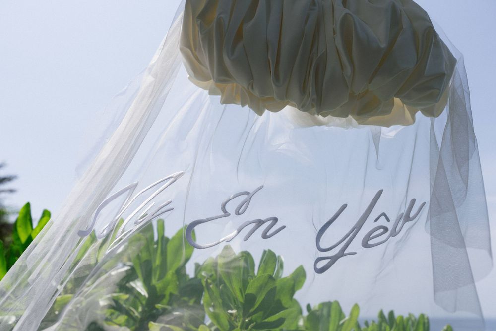 A dreamy outdoor wedding photo series with fluttering white veils against a blue sky and tropical foliage.