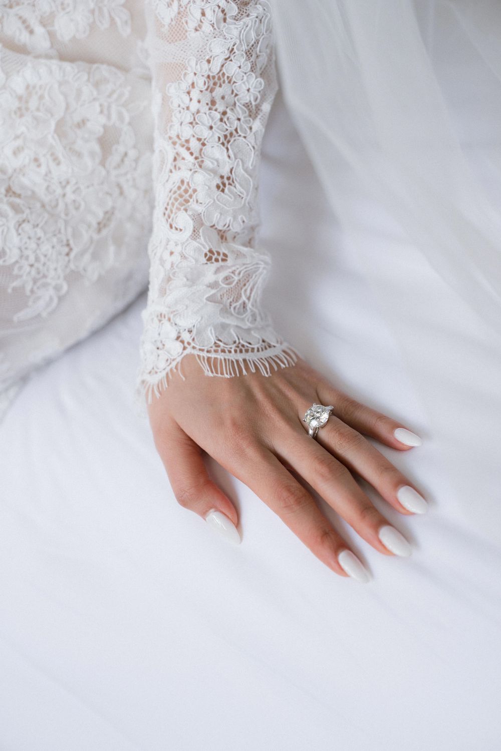 Close up of delicate white lace wedding dress sleeve with manicured hands.