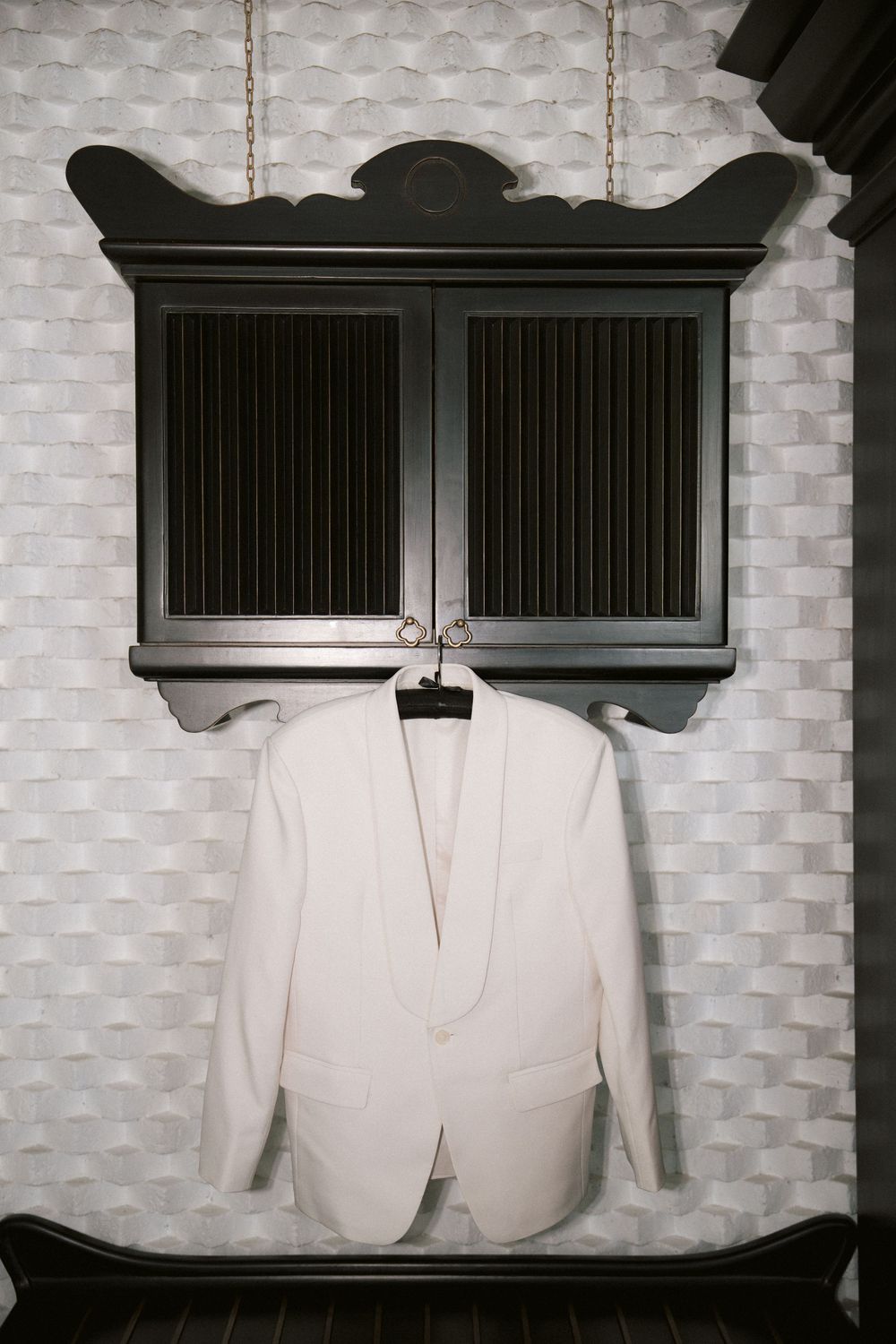 A white formal suit jacket hangs against a textured wall beneath dark wooden cabinet storage.
