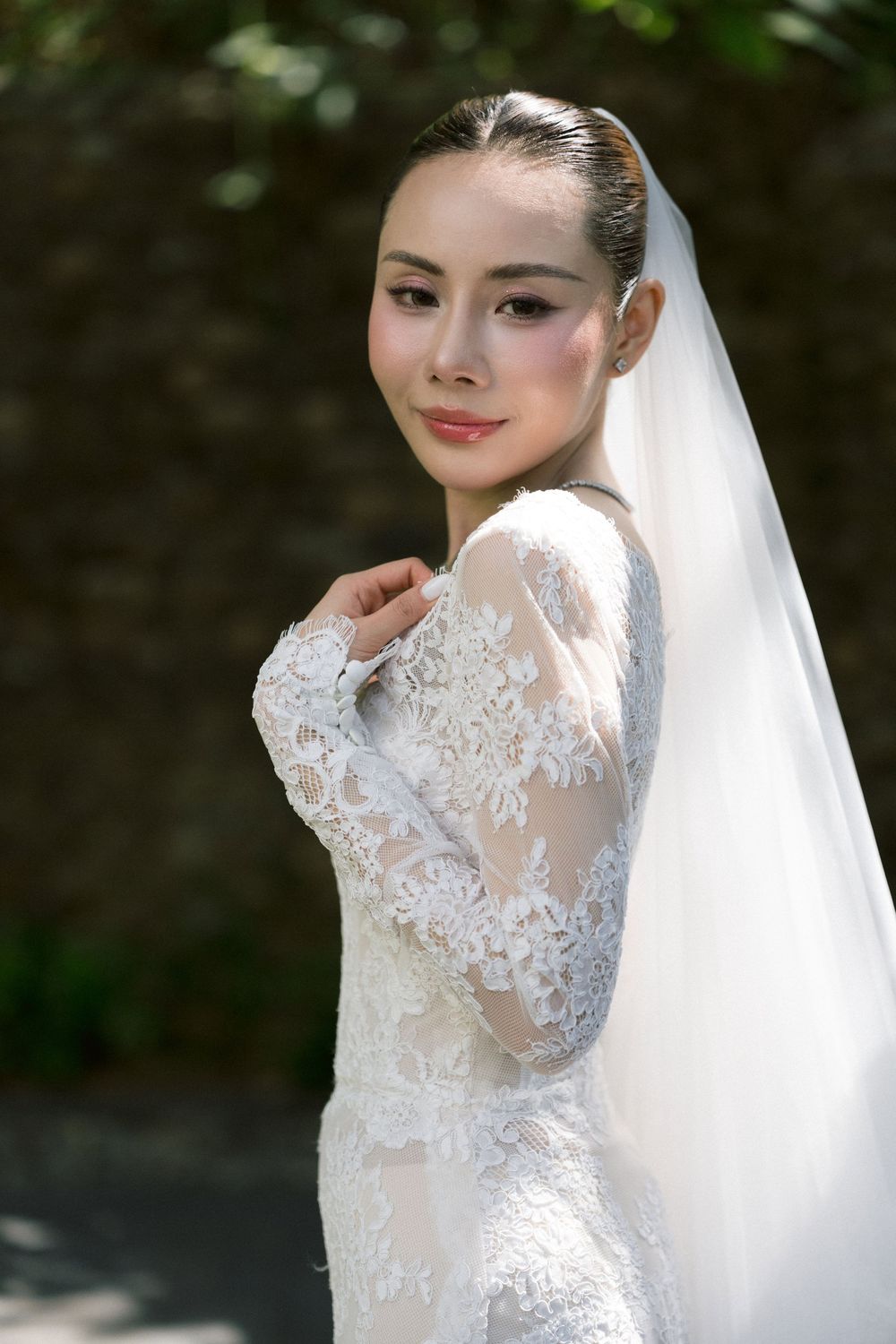 Elegant lace wedding dress with intricate details and flowing veil captured in a close-up portrait shot.
