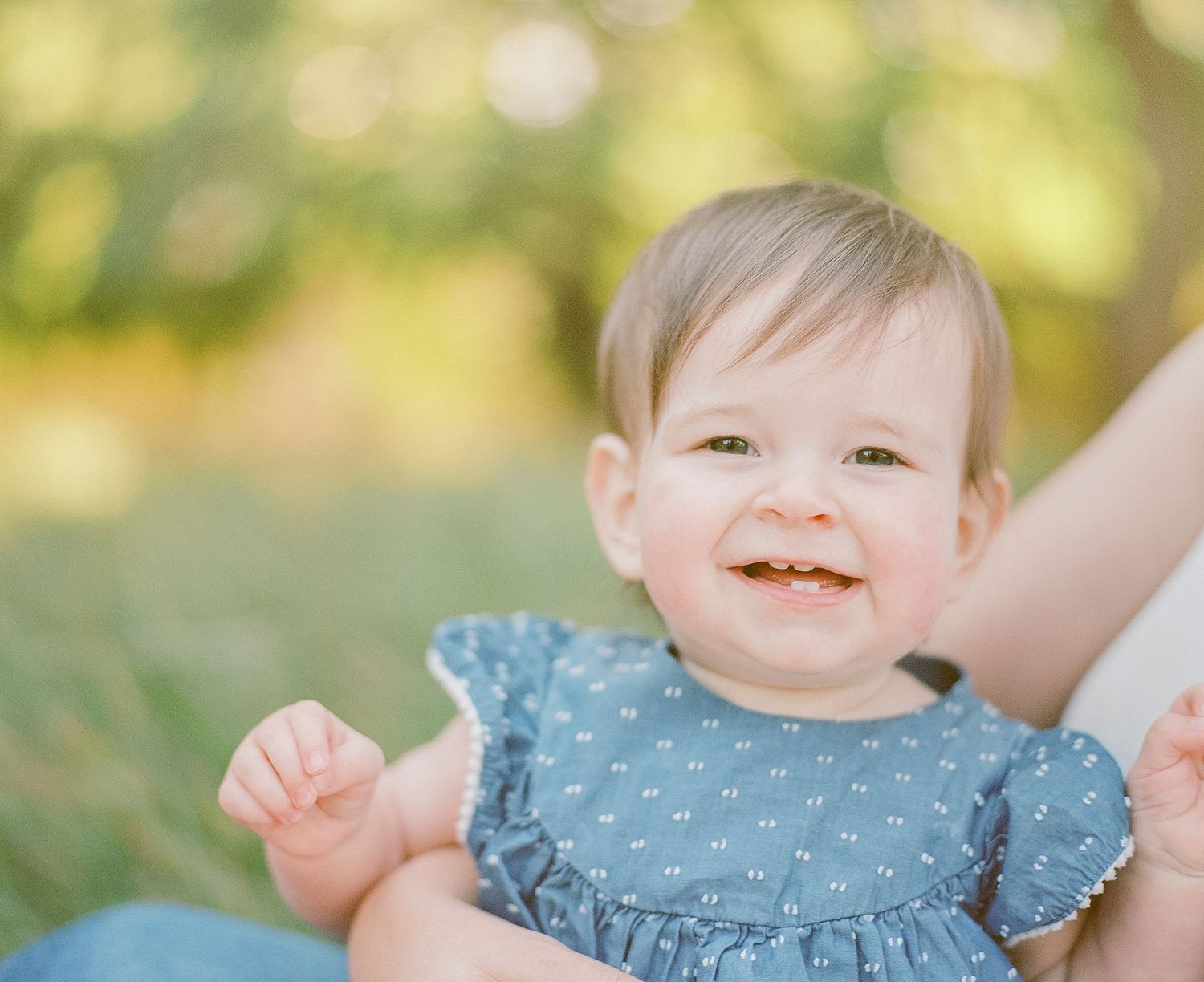 Baby in blue ruffled dress smiling at camera during outdoor photoshoot.