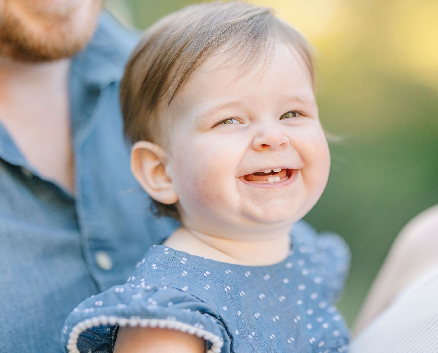 Close-up portrait of a smiling baby wearing a polka dot outfit against a soft natural background.