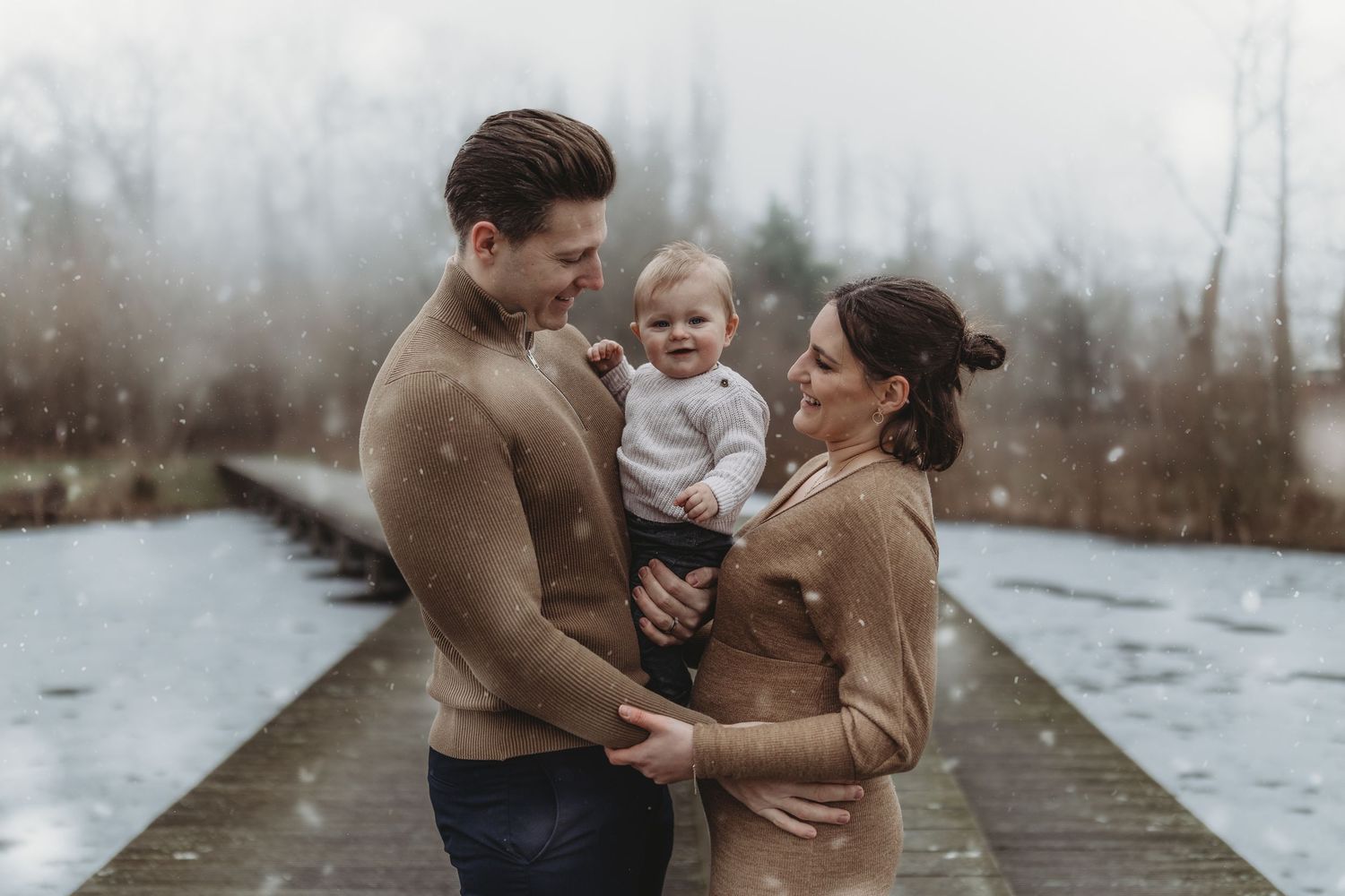 Family enjoying tender moments together along a misty winter path near a lake in earth-tone outfits.