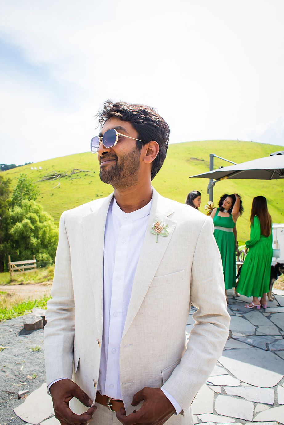Person in a crisp white suit jacket stands against rolling green hills on a bright sunny day, smiling towards the horizon.