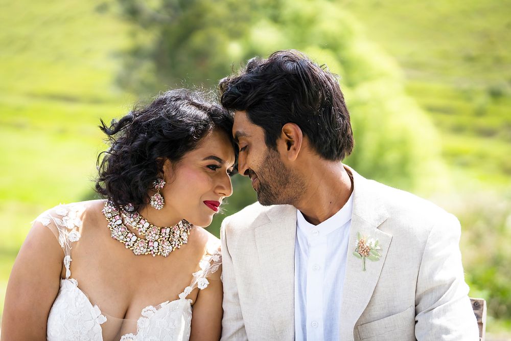 A couple shares a tender moment in white wedding attire against a bright green outdoor backdrop.