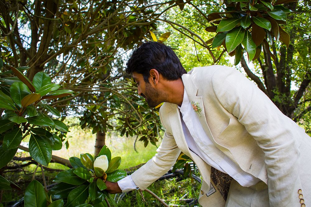 A person in a white shirt carefully inspects leaves and branches in a lush green outdoor garden setting.