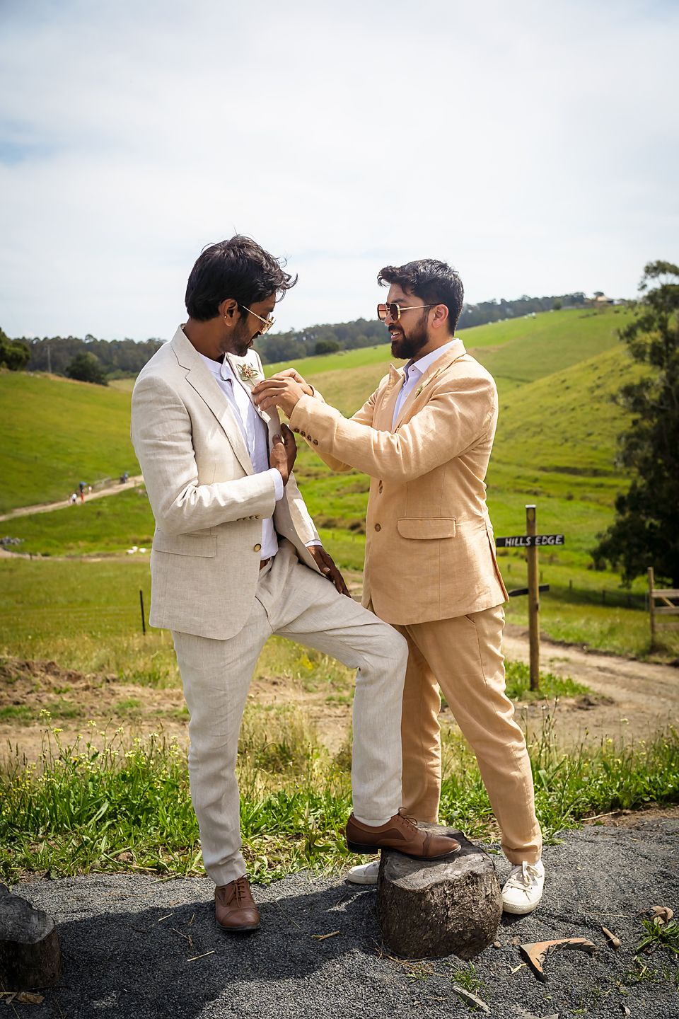 People in light-colored suits posing playfully on rocks with scenic pastoral hills in the background.
