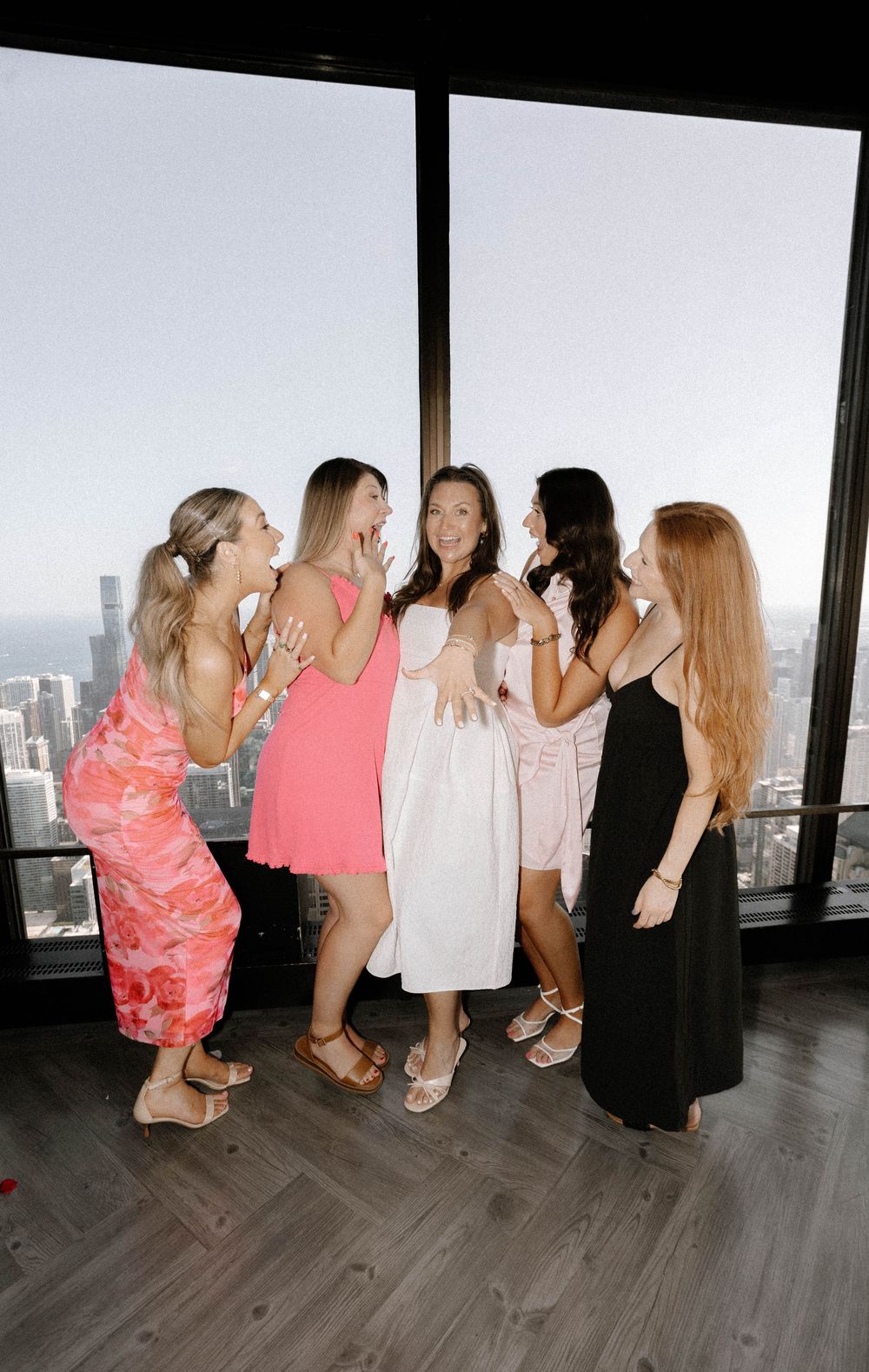 A group of friends in colorful dresses share a candid moment together at a high-rise venue with city views.