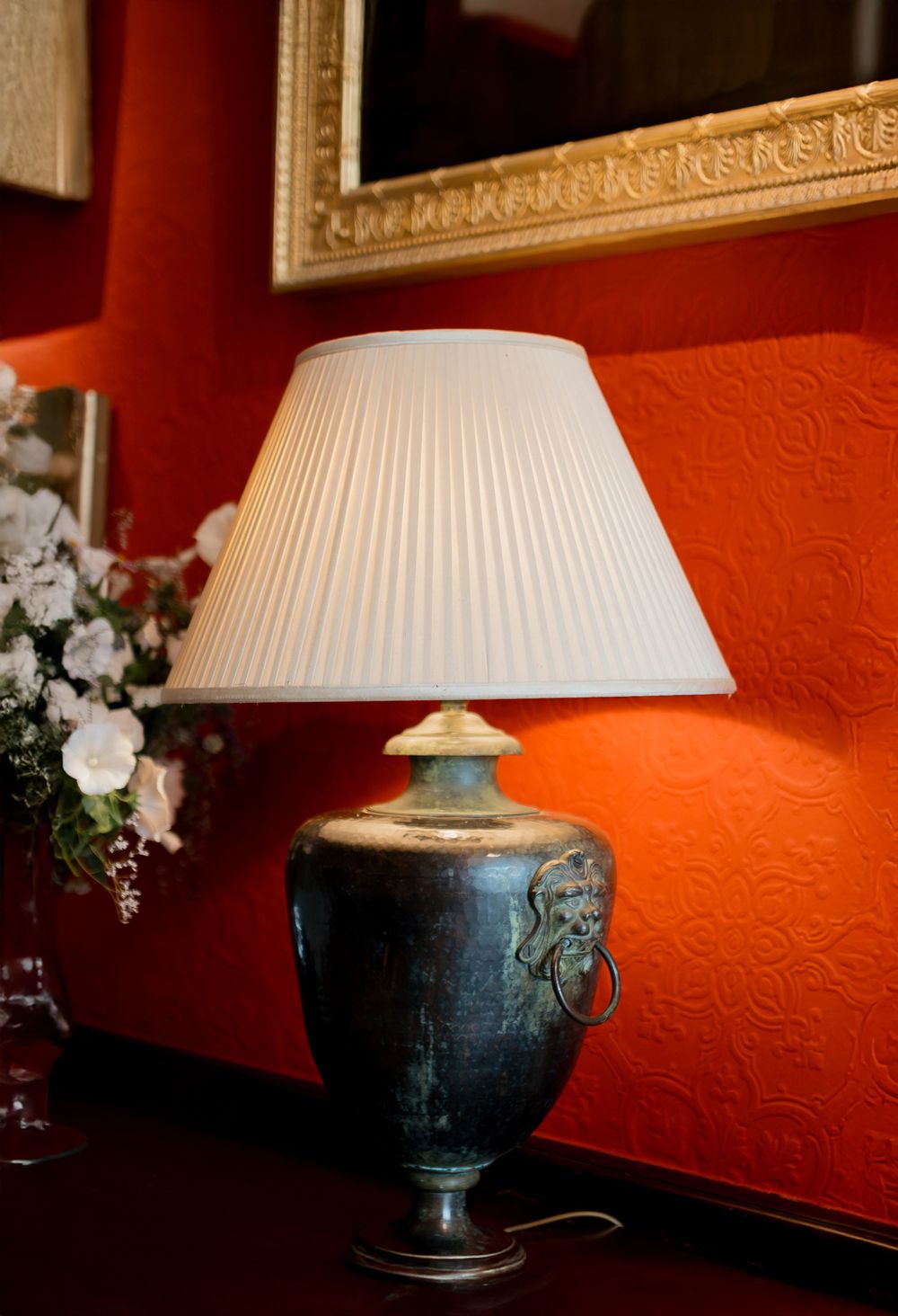 A series of 4 similar lamps with ornate blue ceramic bases and pleated white shades against a textured orange wall.