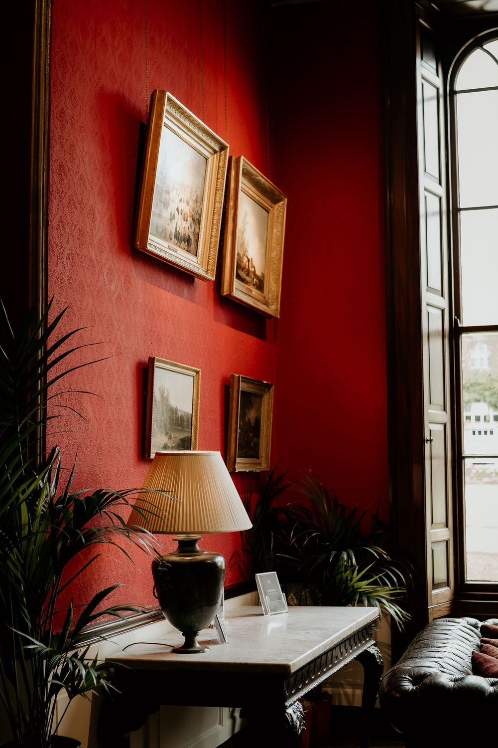 A series of interior shots showing red walls with framed artwork, windows, and potted plants in elegant room settings.
