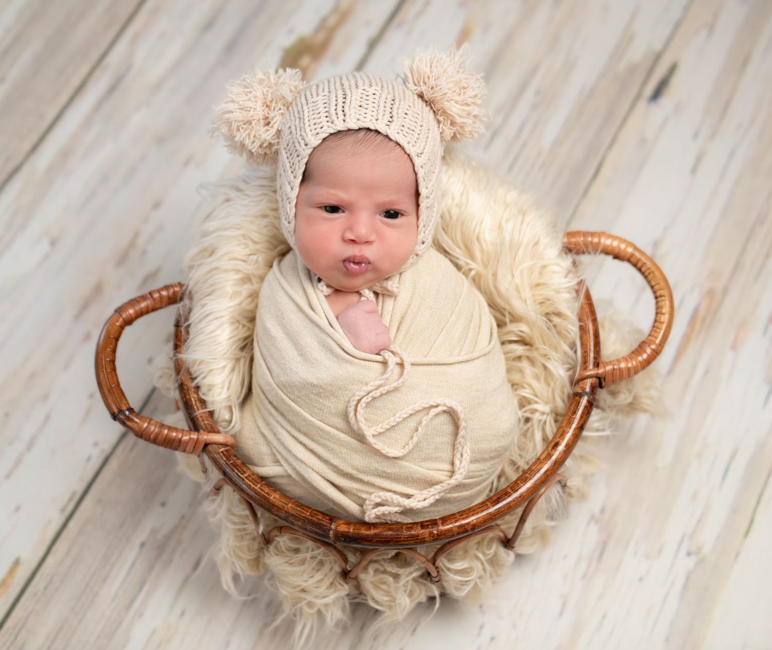 A sleeping baby rests peacefully in a cozy rustic basket with soft cream-colored padding and textures.