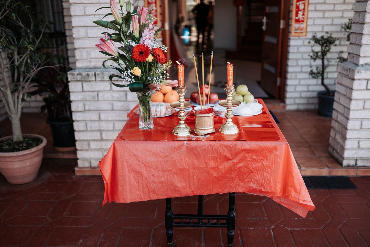 Red tablecloth adorned with flowers, candles and traditional ceremonial items for a Chinese celebration.