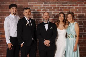 Large wedding party group photo against exposed brick wall background at indoor venue.