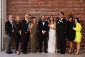 A formal group photo of wedding party members in evening attire posing against a brick wall.