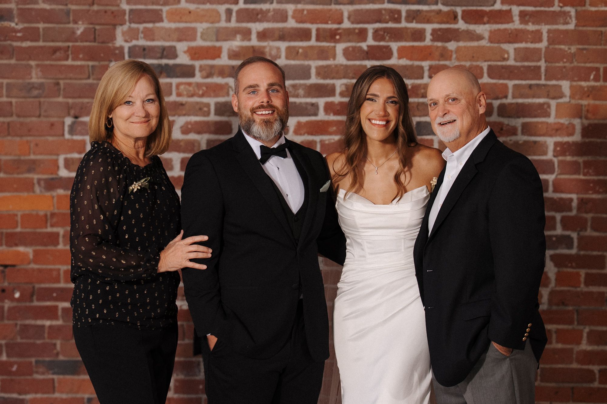Four people stand laughing together against a rustic brick wall background during a photo session.