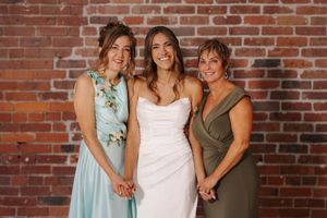 Wedding party poses together in front of rustic brick wall at celebration.