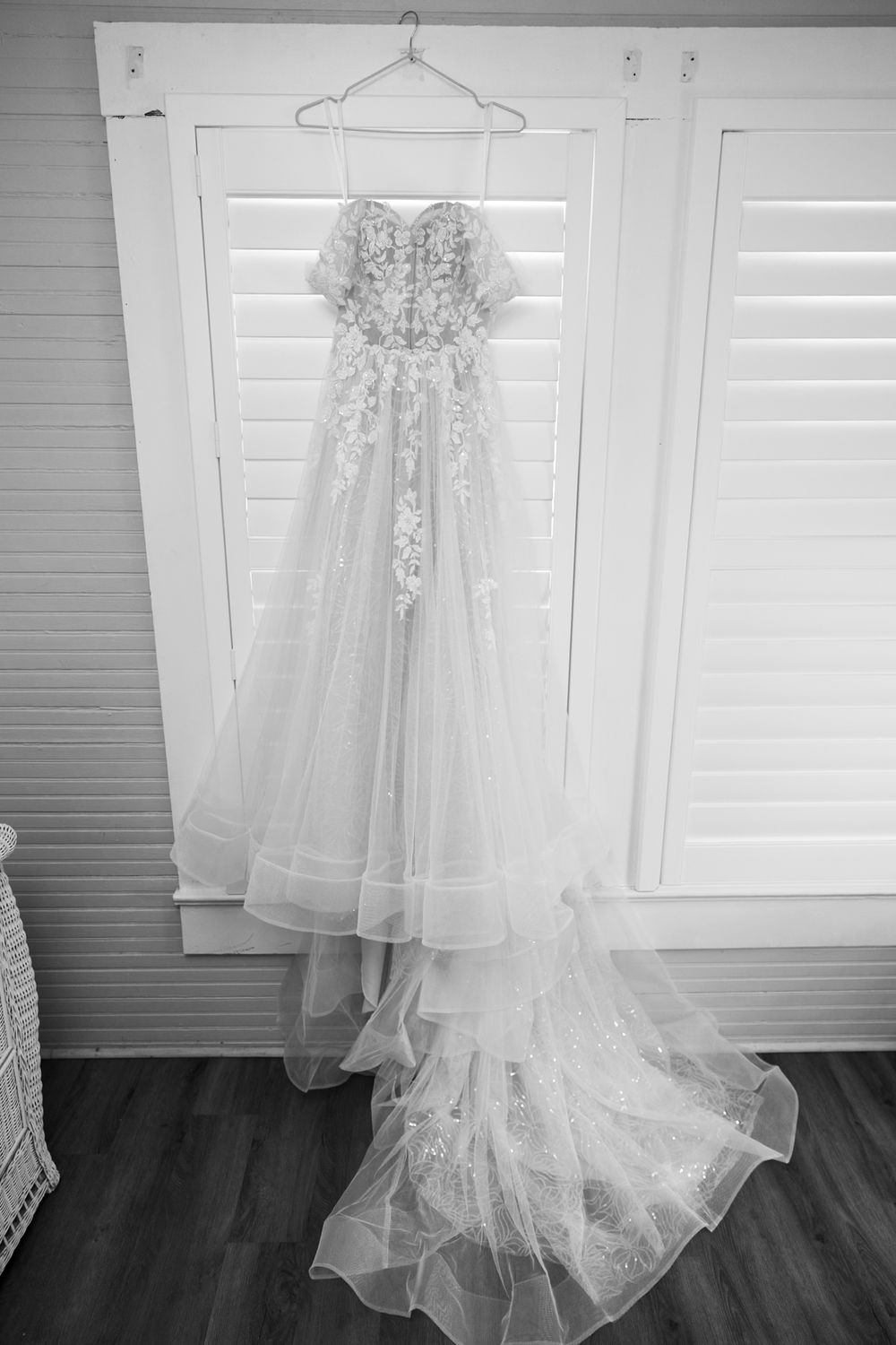 White wedding dress hanging on display against a gray wall with shuttered windows.