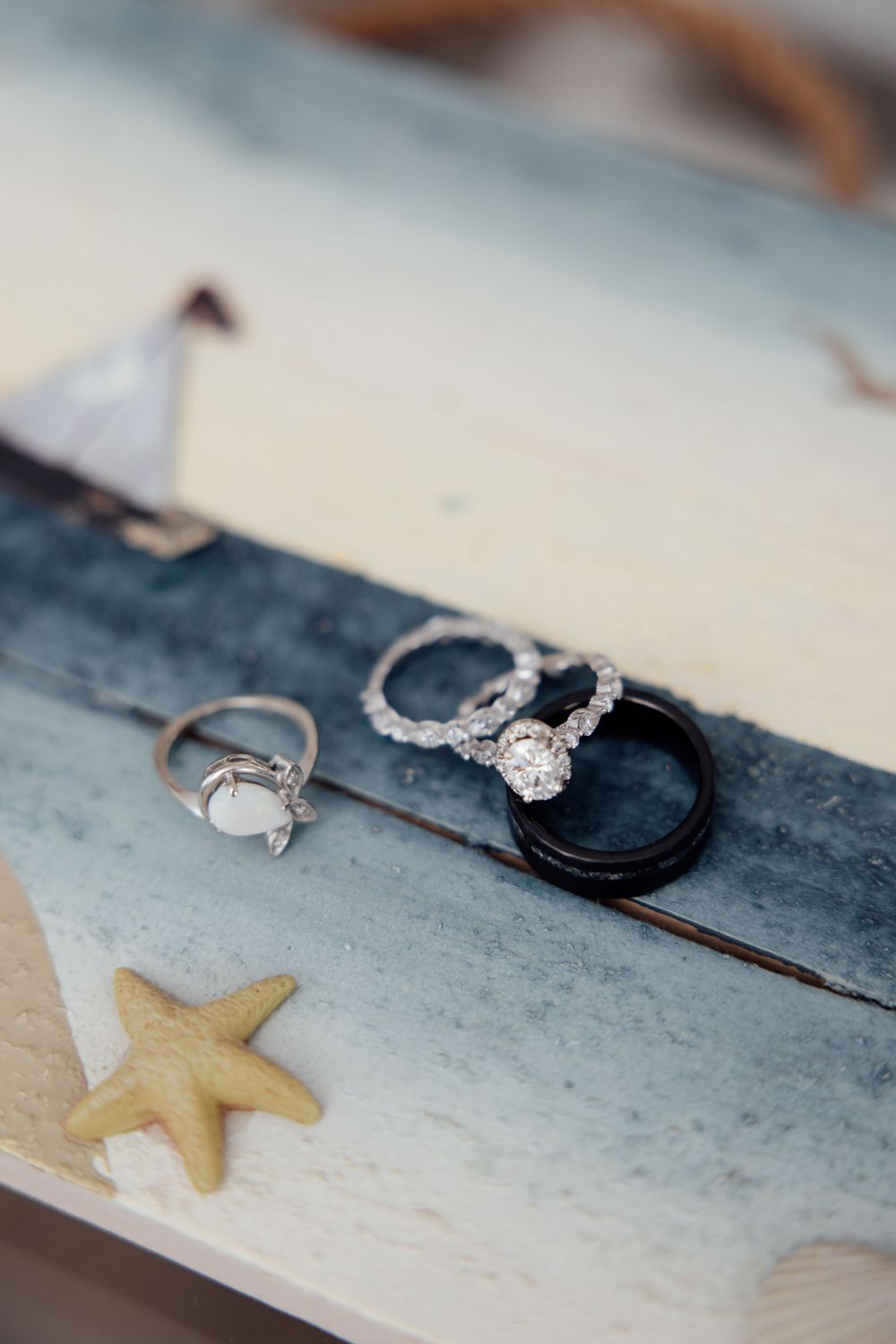 Wedding rings and a starfish arranged on a rustic wooden surface for a beach-themed wedding detail shot.