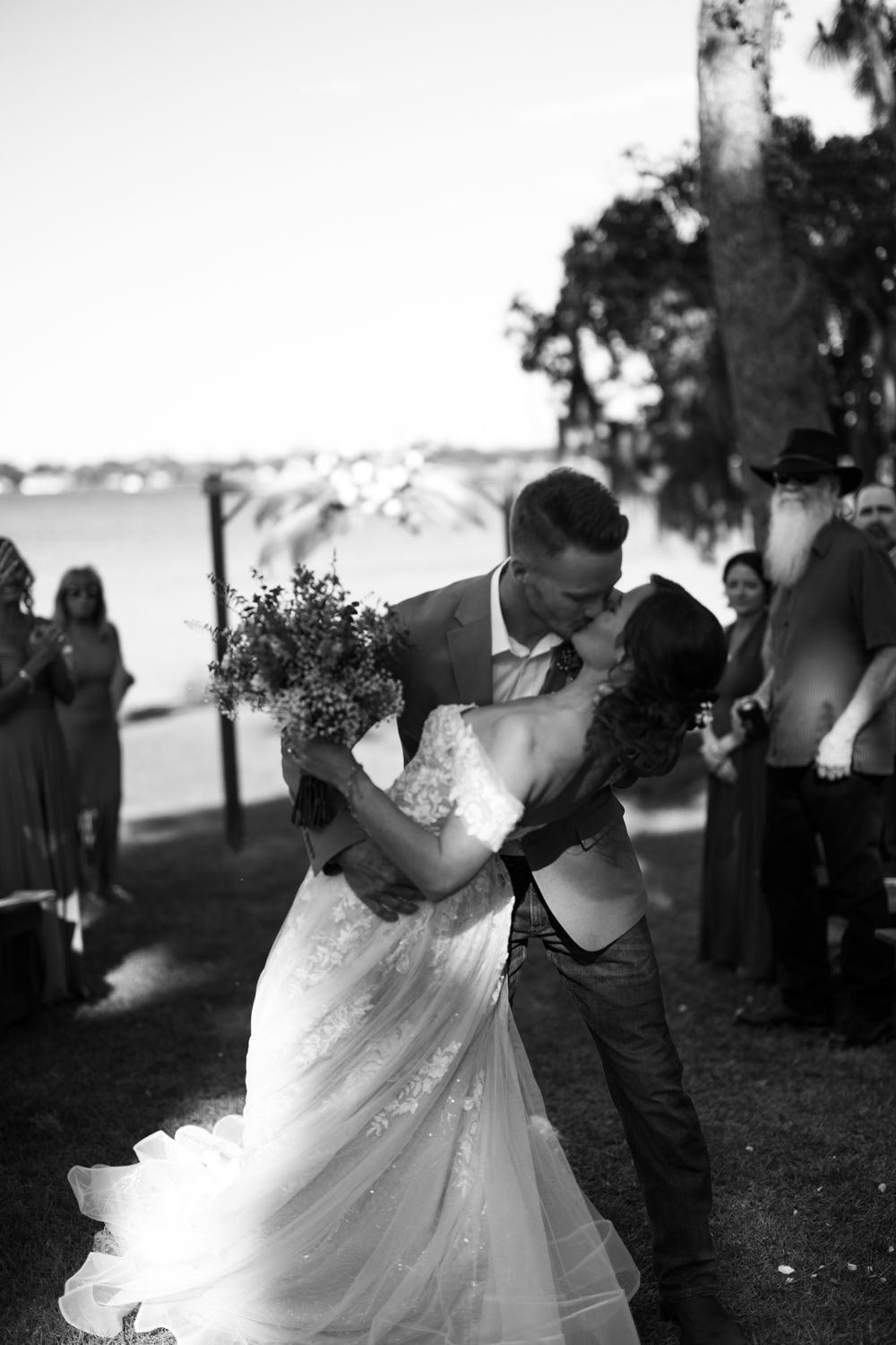 A couple in wedding attire sharing a romantic moment outdoors under trees.
