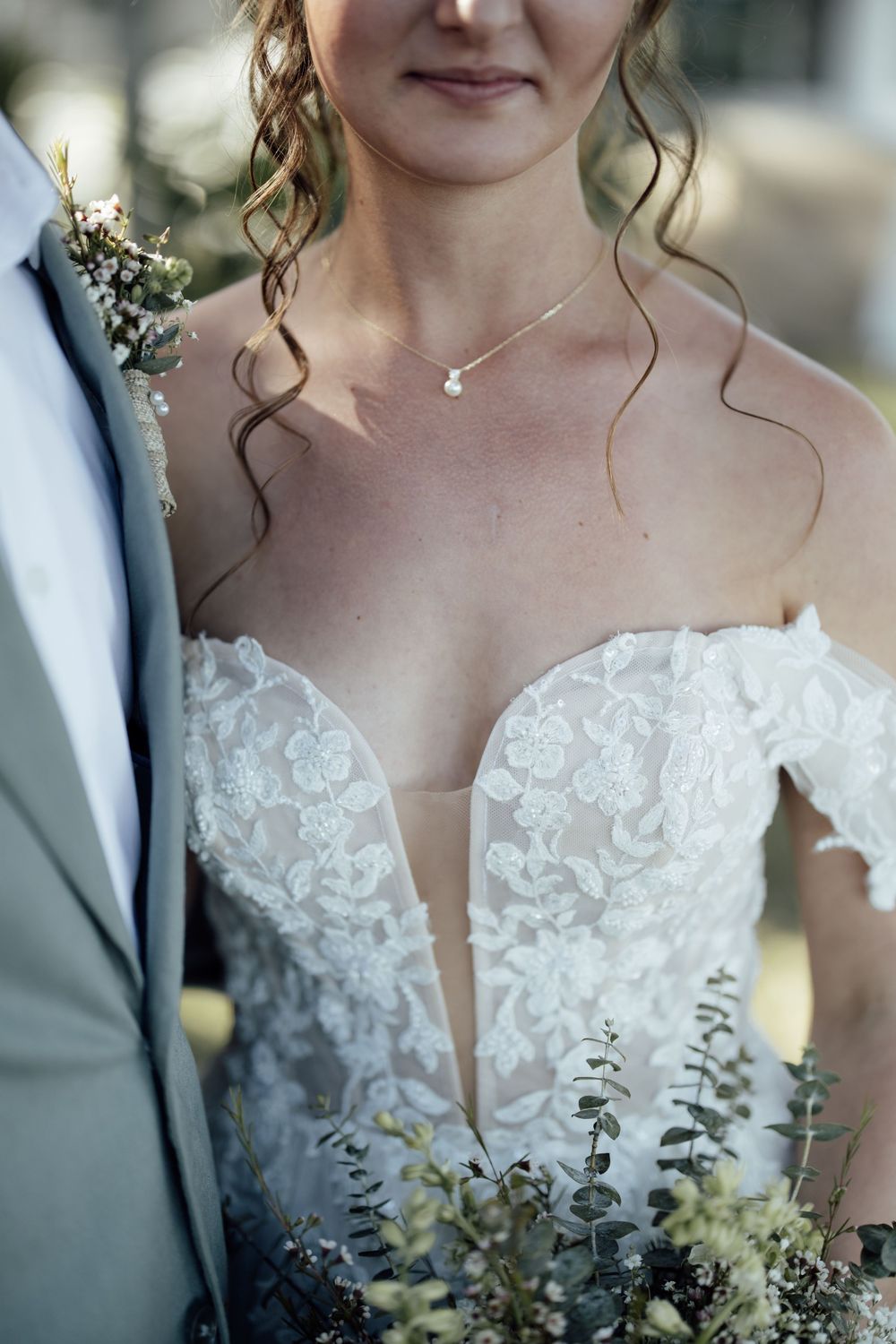 Close-up detail of an elegant white lace wedding dress with floral embellishments.