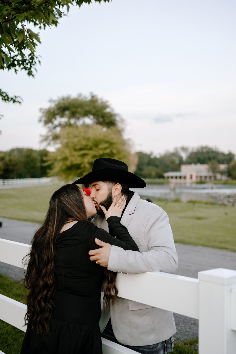 A romantic couple shares tender moments by a white fence in an outdoor setting.