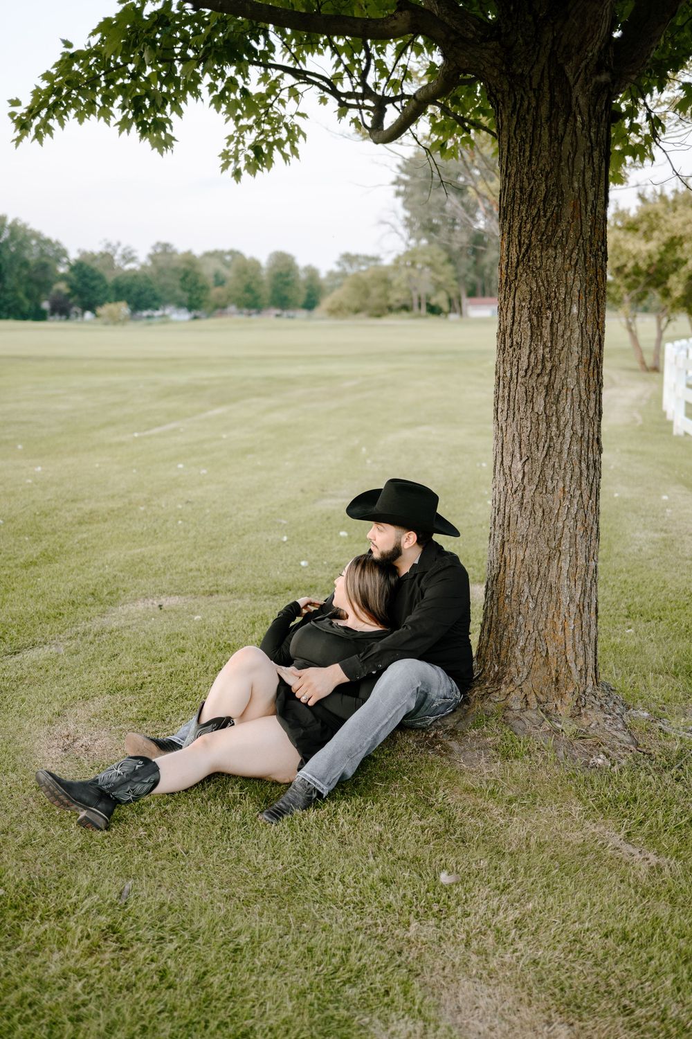 Couple in black clothing lying together under a tree in a peaceful outdoor setting.