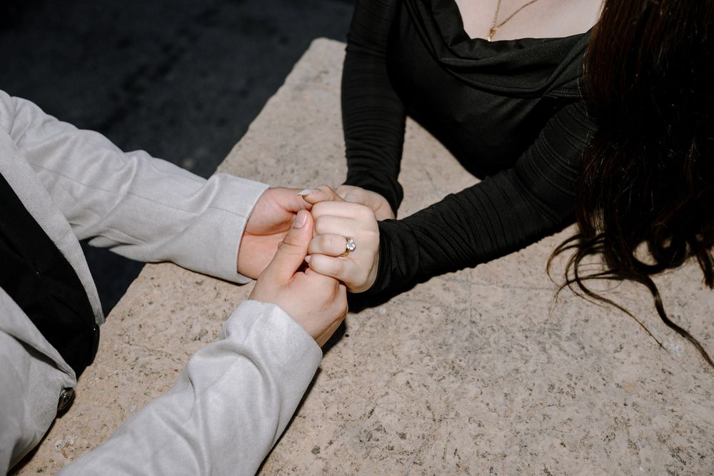 Intimate detail shot of hands holding each other against light colored surface.