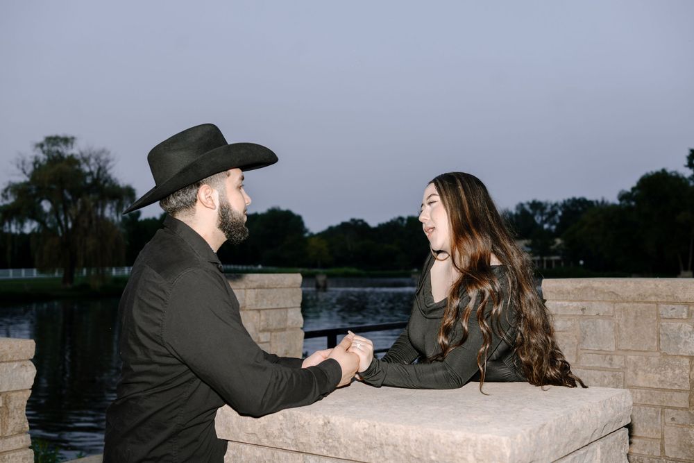 A couple leans against a stone wall overlooking a scenic waterfront view.
