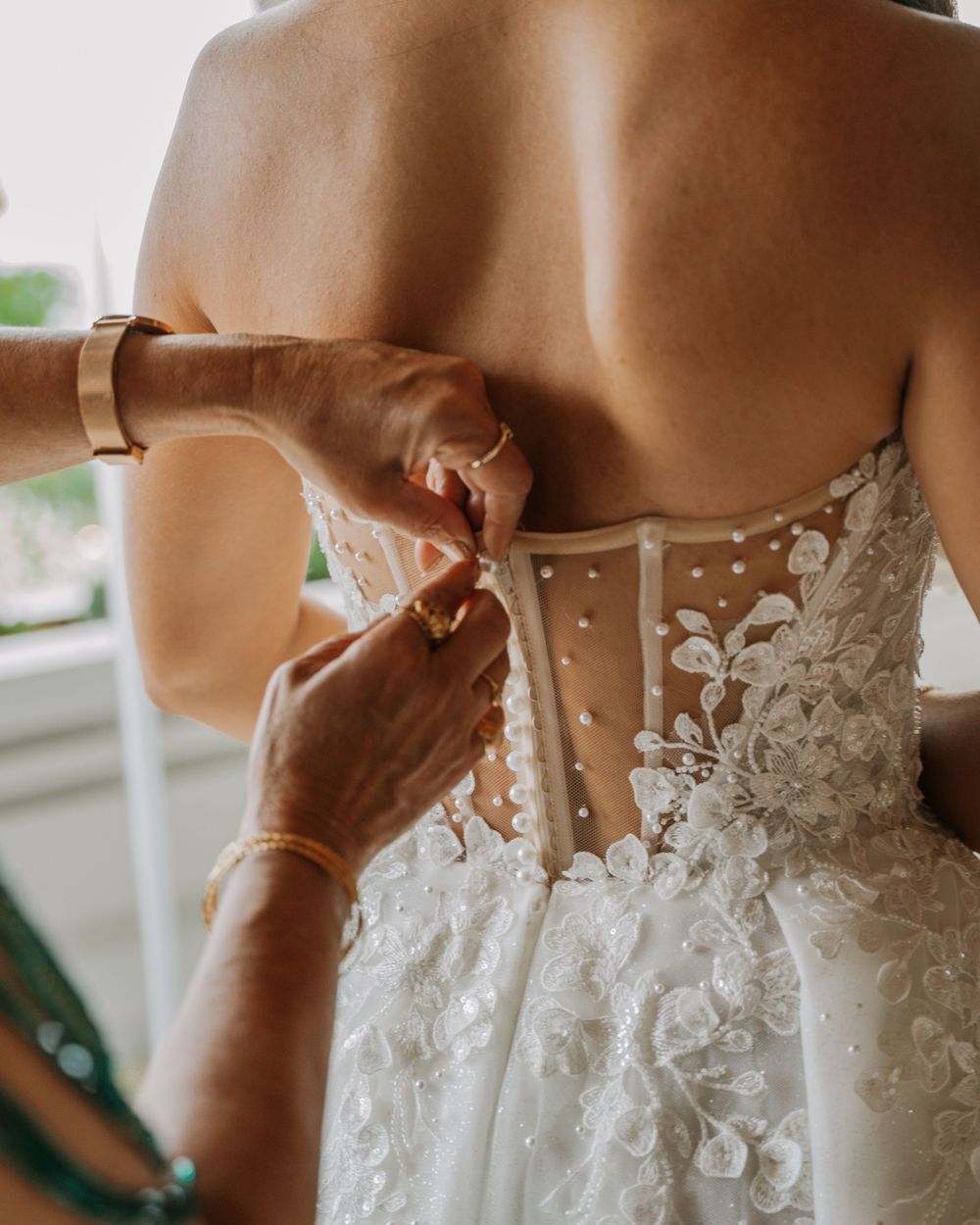Close-up shot of hands adjusting the delicate lace details on the back of a white wedding dress.