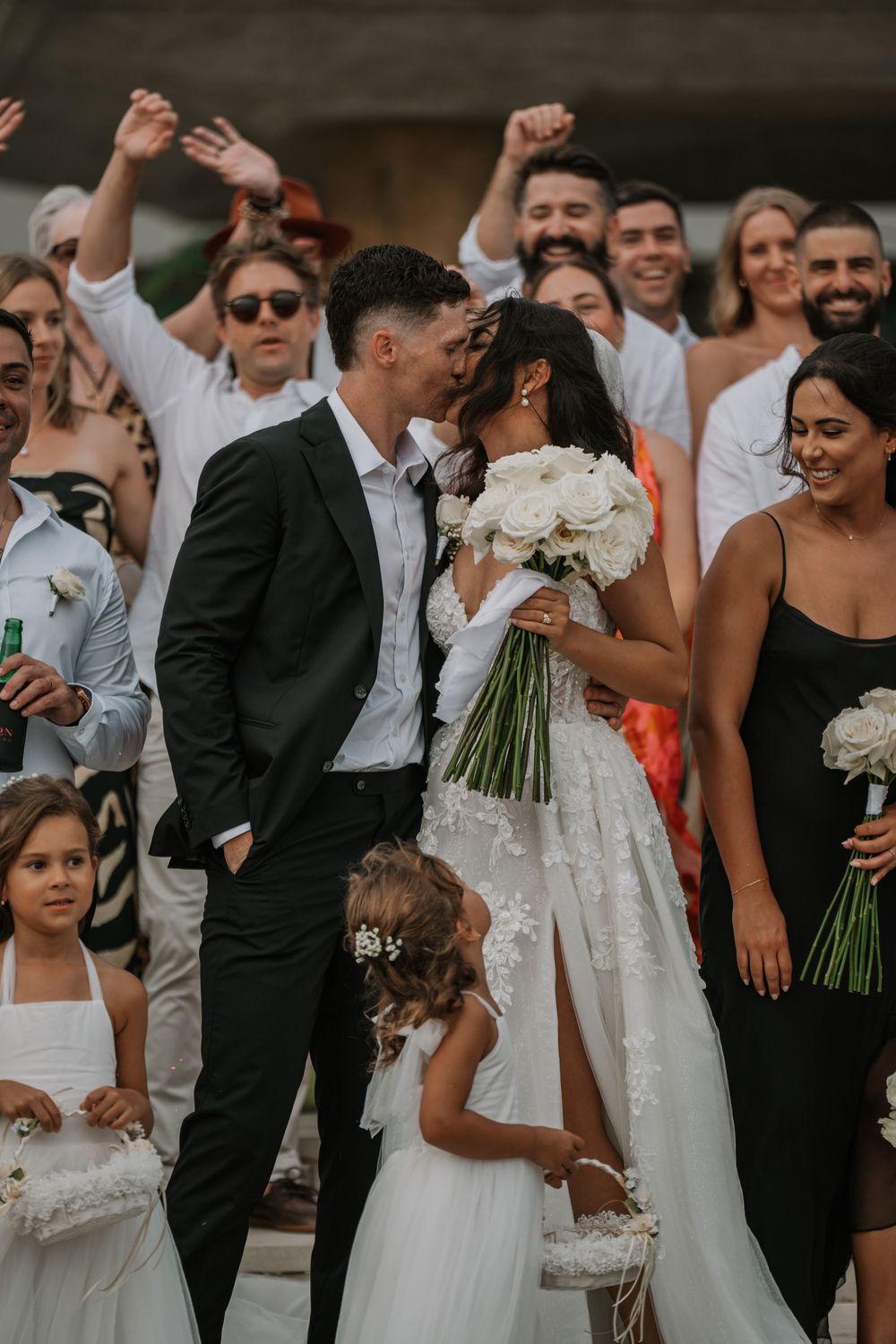Wedding party members gather together for a joyous group photo outside with bouquets and formal attire.