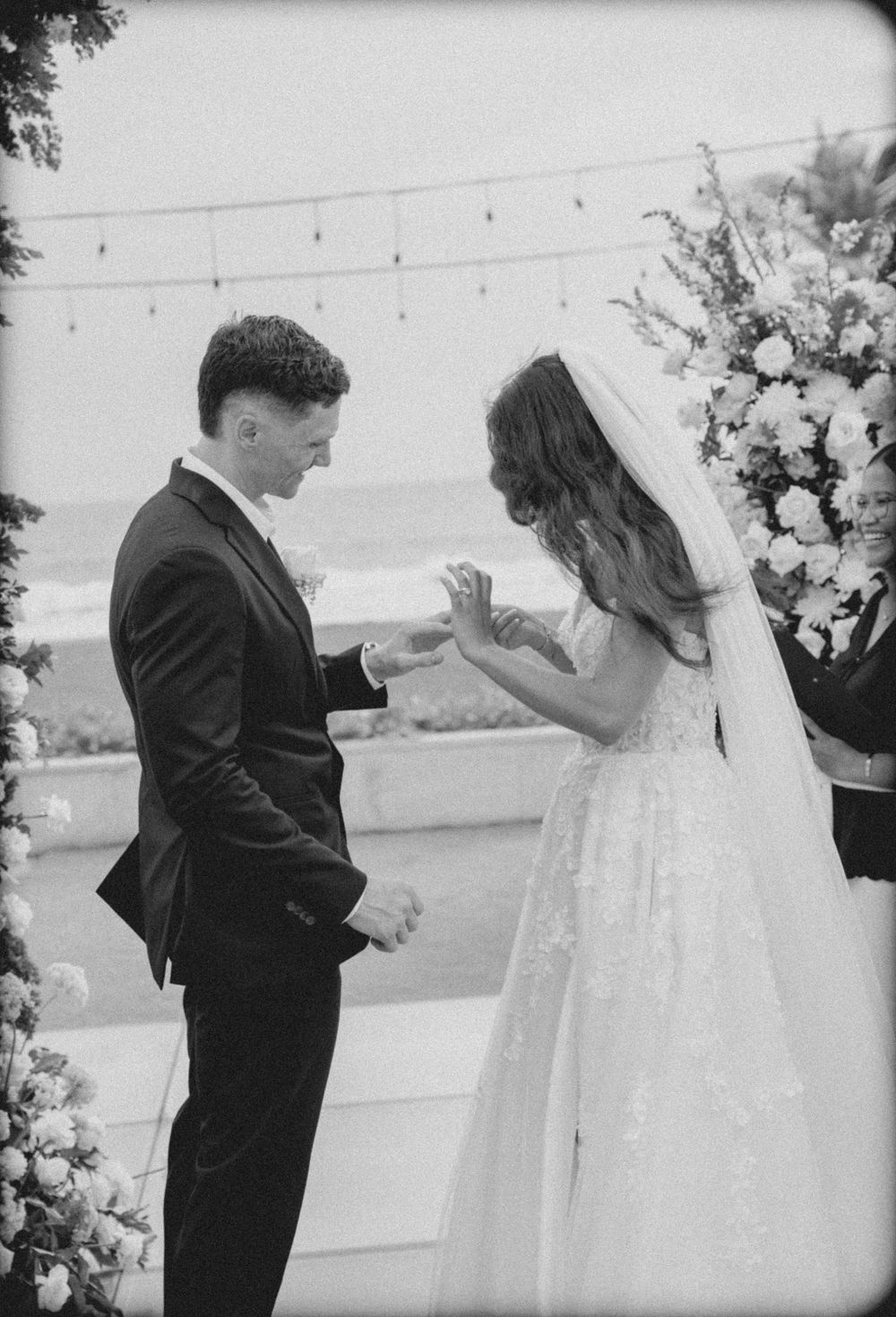 A black and white wedding dance sequence shows a couple swaying together amid floral decorations and string lights.