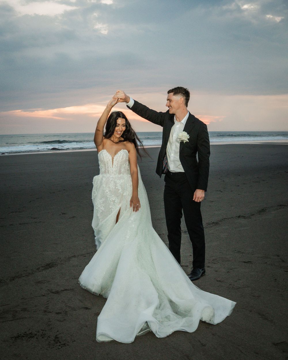 A couple shares a romantic moment on a misty beach at dusk in formal wedding attire.