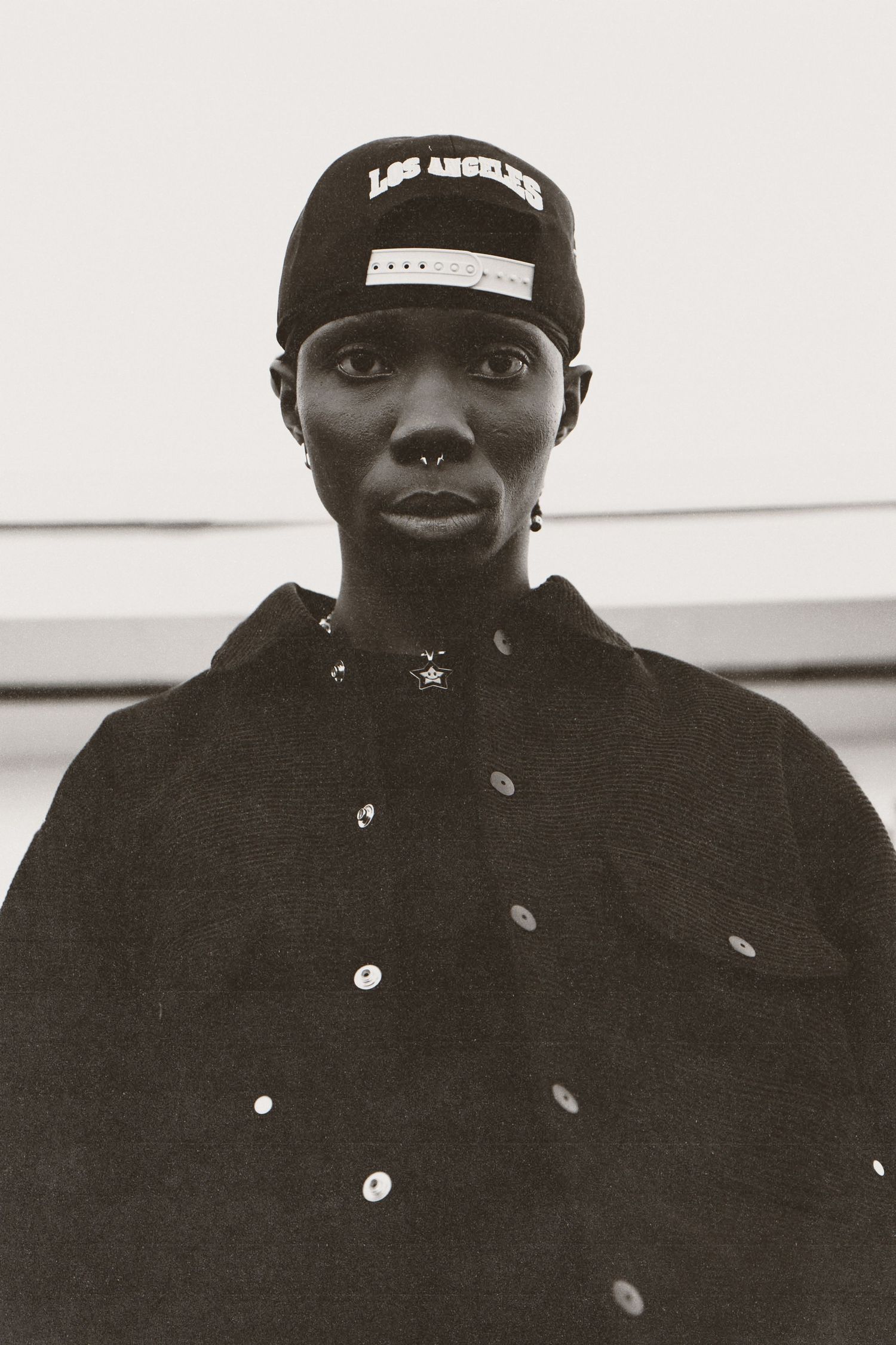 A collage of black and white portraits showing someone wearing a dark baseball cap and jacket with buttons in different poses.