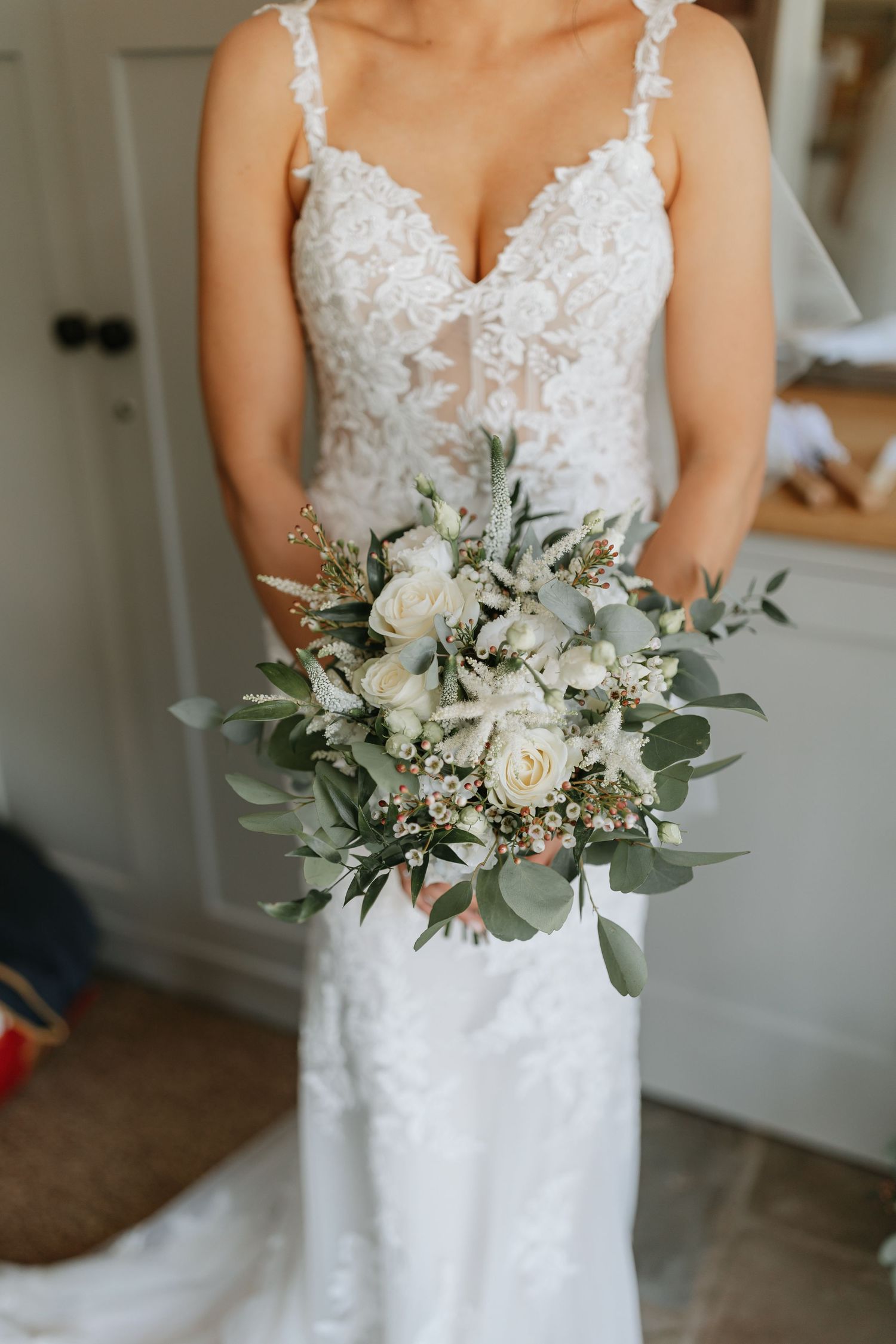 Elegant white wedding bouquet with eucalyptus and roses held against a lace bridal gown gives a romantic and classic look.