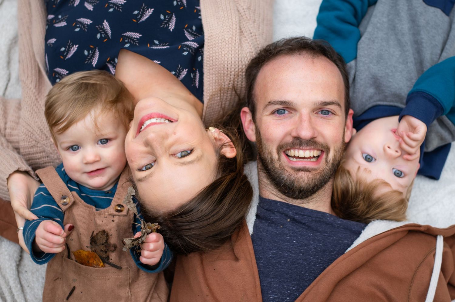 A happy family lies together on a wooden floor while smiling warmly at the camera.