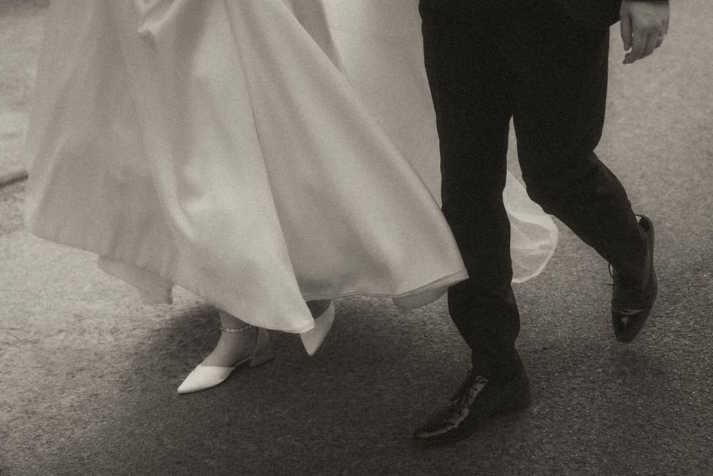Black and white photo of wedding dress and suit legs walking together on a paved surface.