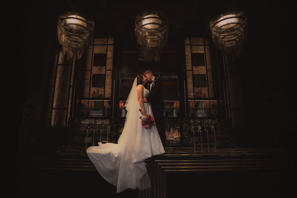 A couple in wedding attire shares a romantic dance in a dimly lit historic venue with elegant architecture.