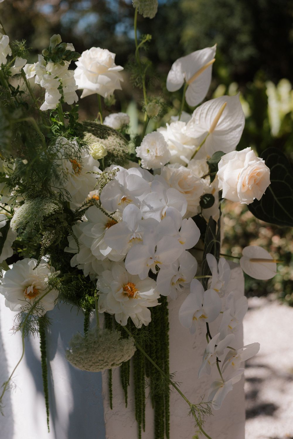 Elegant white orchids and delicate greenery arranged in a cascading display along a white railing in a garden setting.