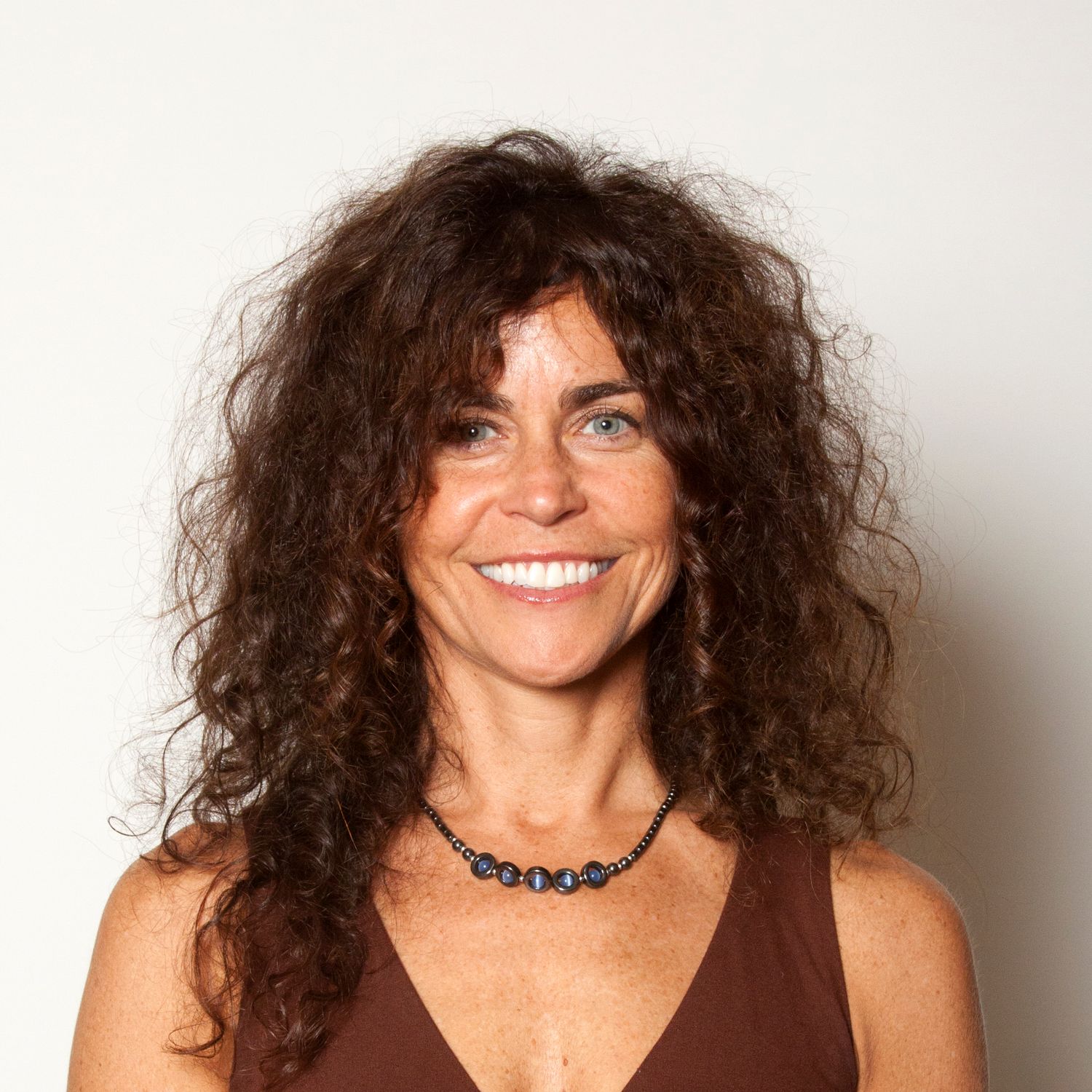 Headshot of a woman wearing a brown tank top and necklace with long curly hair.