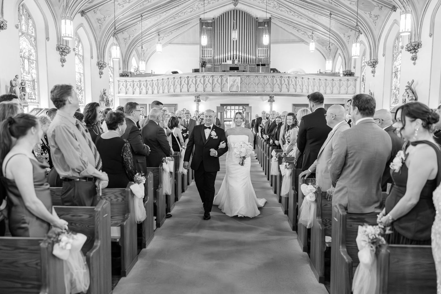 A couple walks down the aisle of a grand church with ornate architecture and a pipe organ during a wedding ceremony.