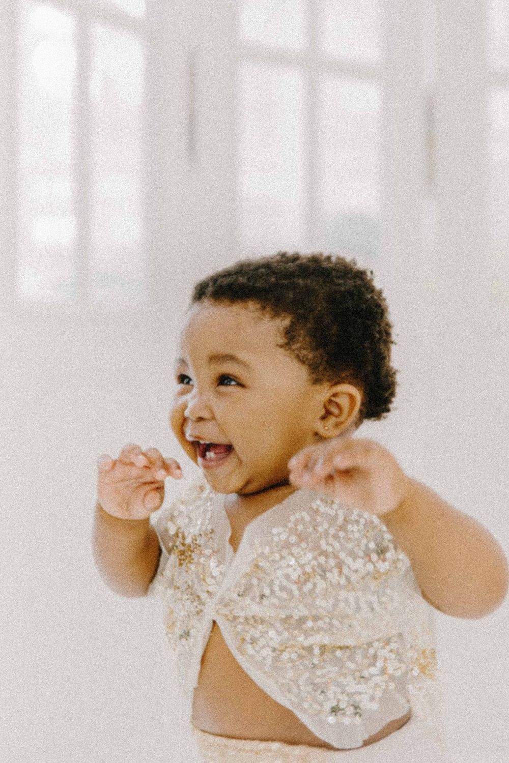 Joyful toddler wearing lace outfit laughing against white background. Book professional maternity, newborn, and family photography.