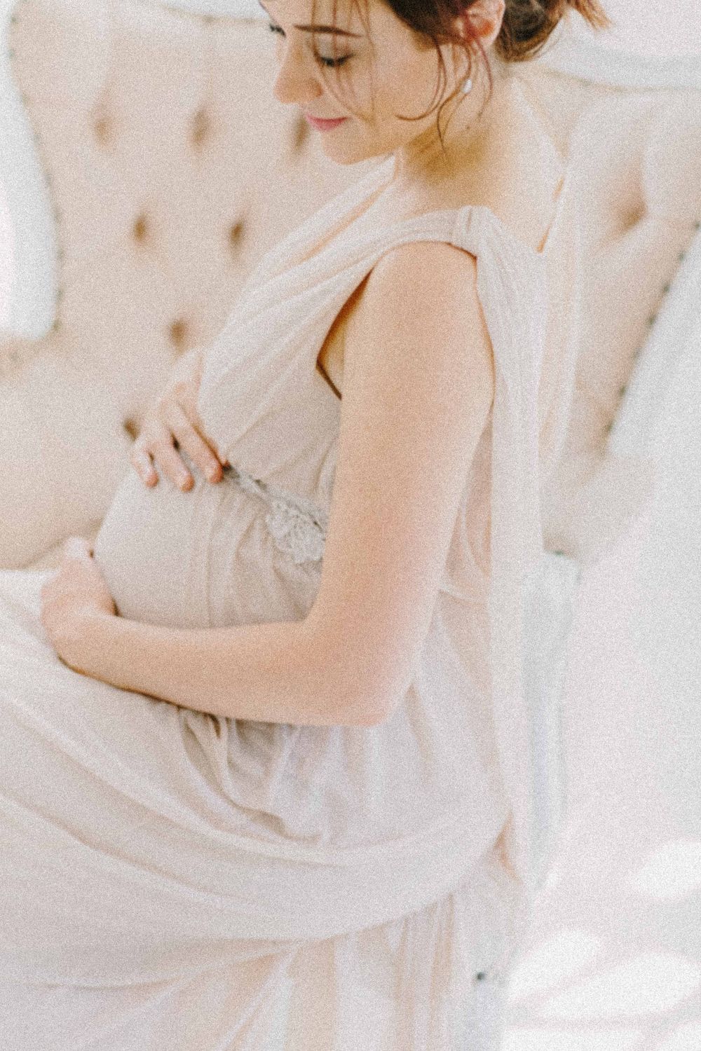 Side view of pregnant woman in soft white dress touching her belly. Book professional maternity, newborn, and family photography in Alenquer