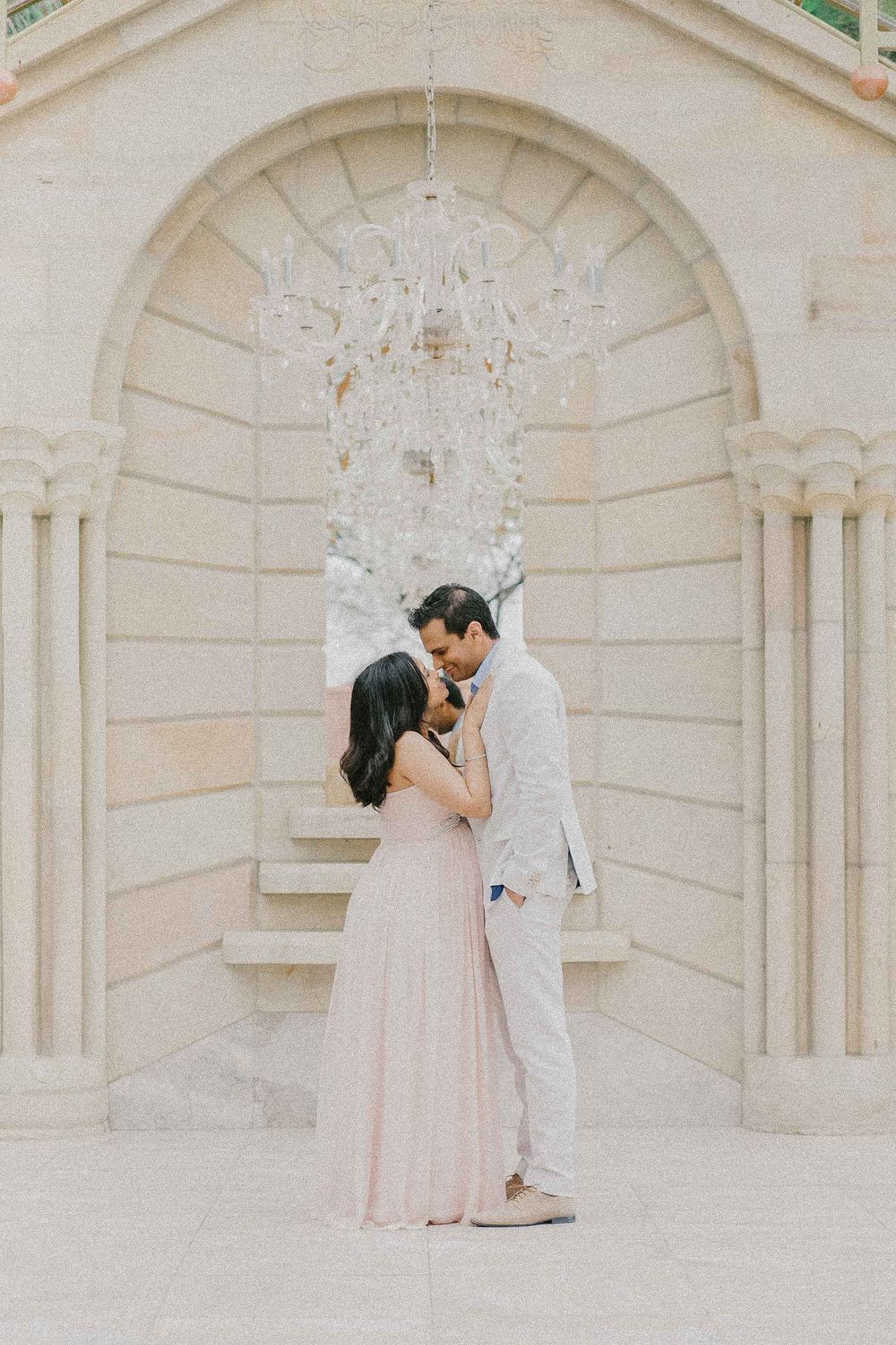 Romantic couple shares tender moments against elegant architectural backdrop.